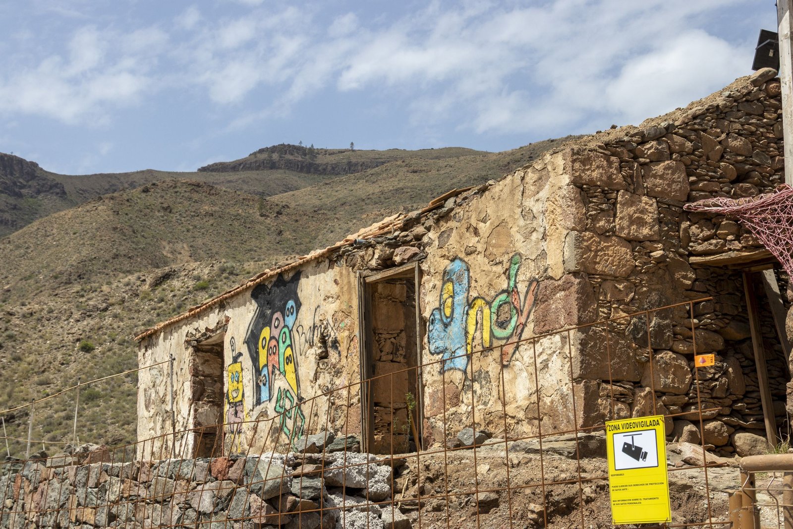 An old stone house with colorful graffiti in a rural, mountainous setting.