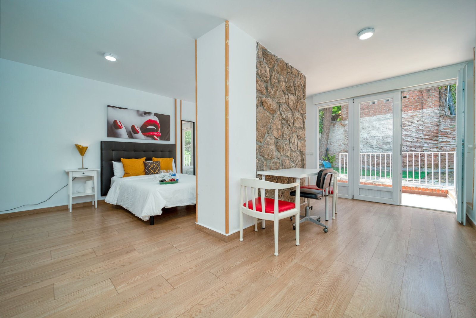 Stylish minimalist bedroom with stone partition and natural light, featuring wooden floors and modern decor.